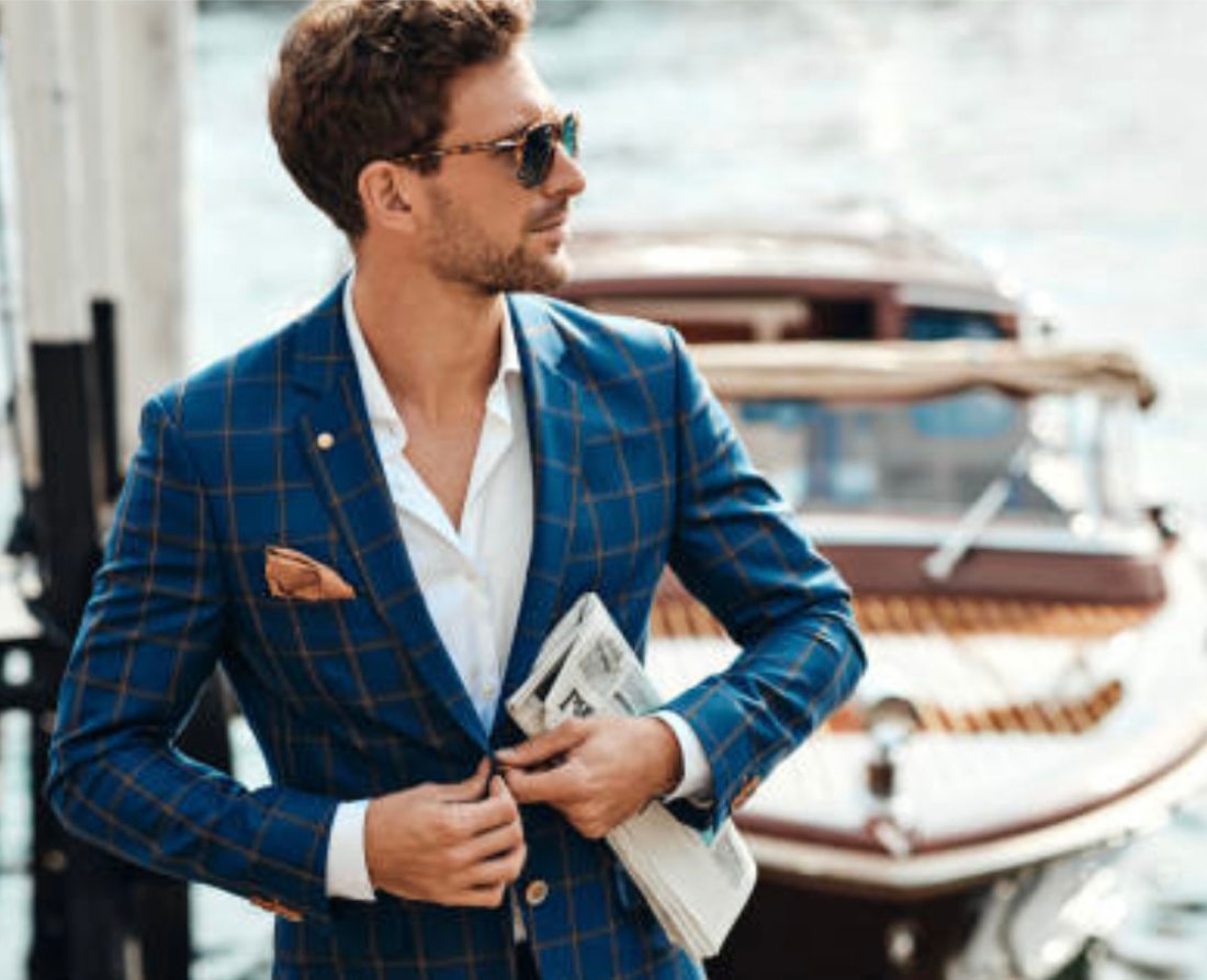 Confident, well-dressed man in suit with newspaper in hand and luxurious boat in background