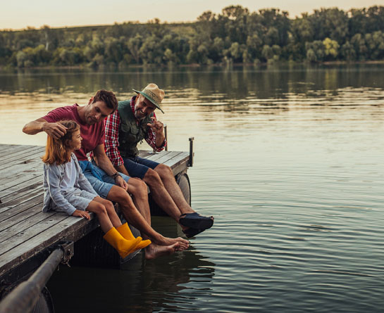 Three generations – grandfather, father, daughter sitting on a dock at a lake